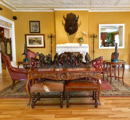 A cozy room with a wooden table, horse sculptures, vintage chairs, and a buffalo head mounted on the wall.
