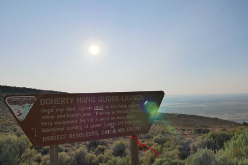 Sign for Doherty Hang Glider Launch with sun shining above, overlooking a vast landscape and sagebrush.