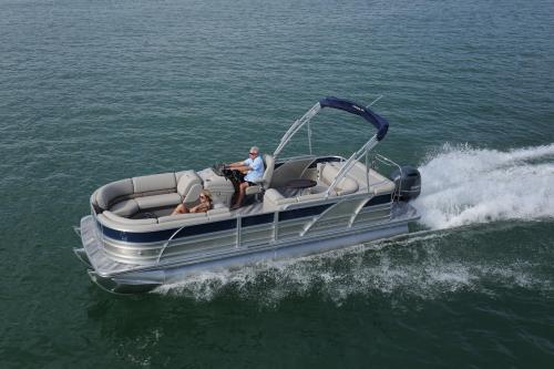 A pontoon boat speeds across the water with two people onboard, enjoying a sunny day.