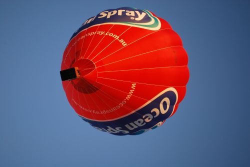A vibrant red hot air balloon with "Ocean Spray" branding floats against a clear blue sky.