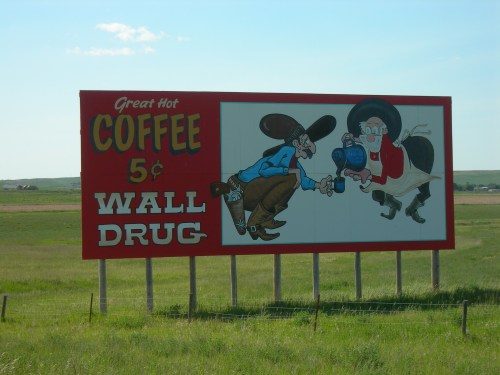A colorful billboard advertising 5¢ coffee at Wall Drug, featuring cartoon cowboys and a playful design.