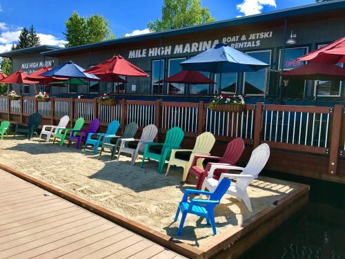 Colorful beach chairs line a sandy area in front of a marina with umbrellas and a rental shop.