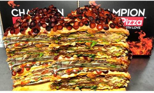 A towering stack of layered pizza with pepperoni, vegetables, and various toppings, next to pizza boxes.