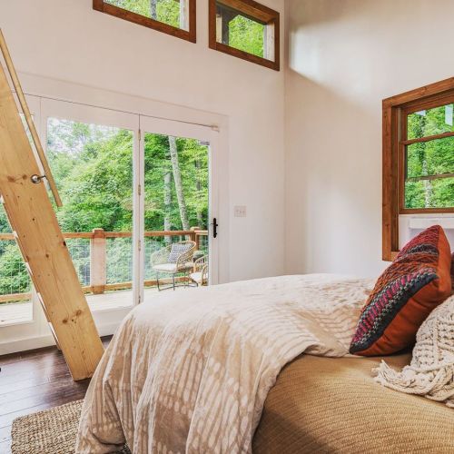 Cozy bedroom with a large window, wooden accents, and a view of lush greenery outside.