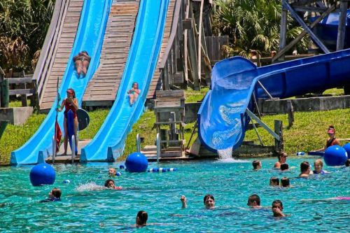 A water park scene with two blue slides, swimmers in a pool, and a lifeguard on duty.