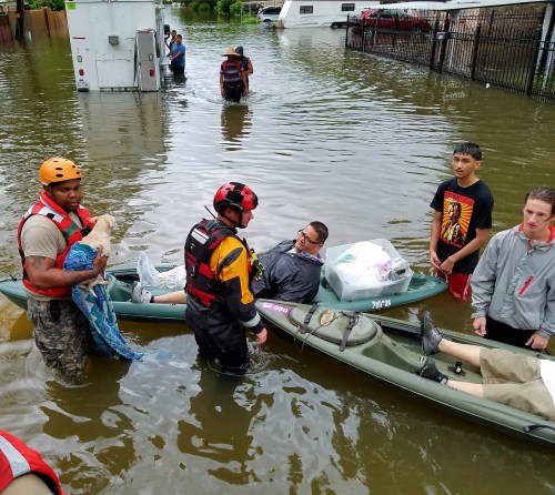 Rescue workers assist individuals in flooded waters, using kayaks and providing support to those in need.