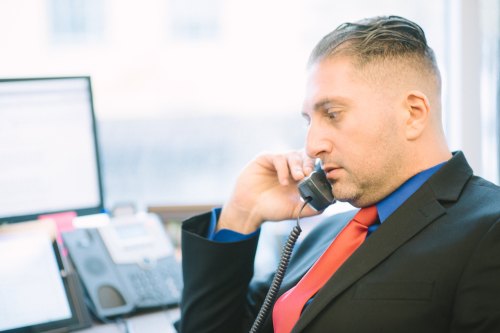 A man in a suit talks on the phone at an office desk, focused on his conversation.