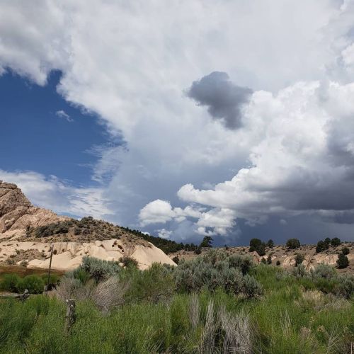 A scenic landscape featuring rocky hills, lush greenery, and a dramatic sky with clouds.