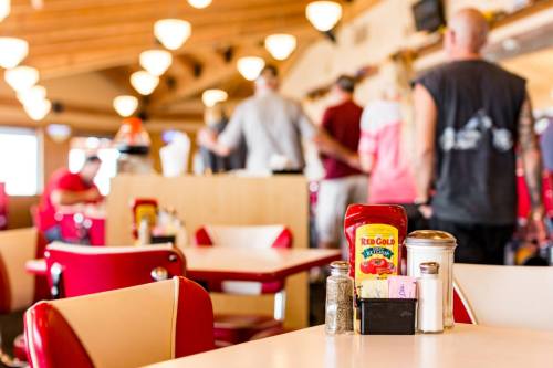 A diner table with condiments in the foreground, blurred patrons in the background, and retro decor.