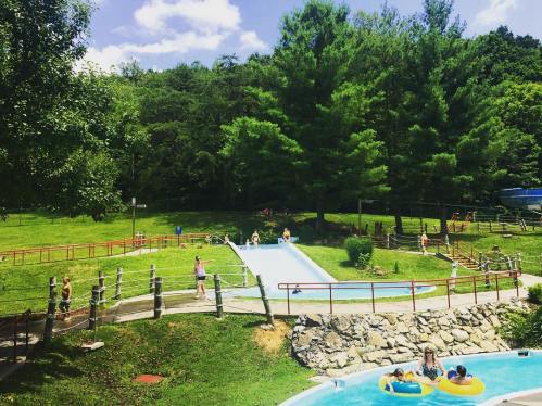 A sunny outdoor water park with slides, pools, and people enjoying the day surrounded by green trees.