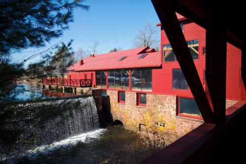 A red building beside a waterfall, surrounded by trees and clear blue skies.