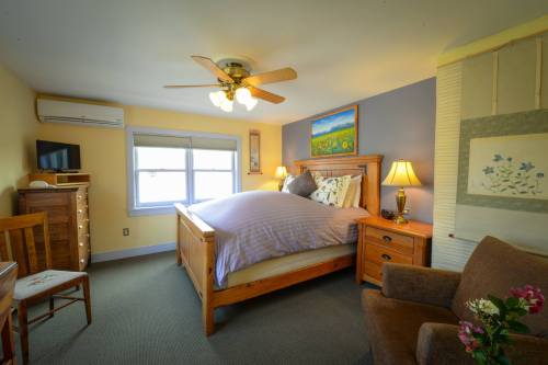 Cozy bedroom with a wooden bed, dresser, TV, and a chair, featuring soft lighting and colorful wall art.