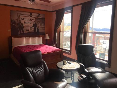 Cozy hotel room with a red bedspread, two armchairs, and large windows showcasing a mountain view.