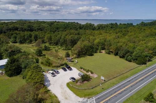 Aerial view of a parking area surrounded by trees, with a road and a body of water in the background.