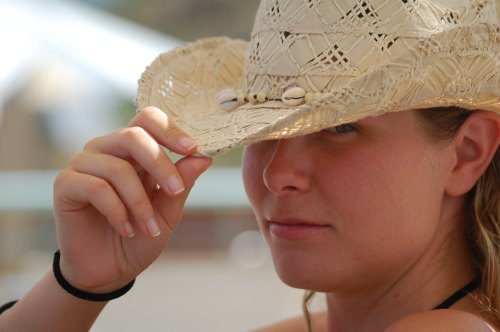 A woman wearing a straw hat, partially shielding her face, gazes thoughtfully at the camera.