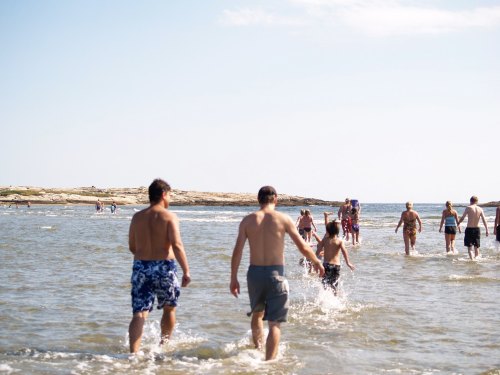 People wade through shallow water at the beach on a sunny day, enjoying the warm weather and ocean.