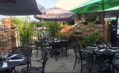 Outdoor dining area with black metal tables, umbrellas, and a decorative fountain surrounded by greenery.