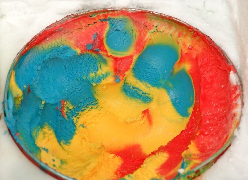 A colorful swirl of blue, yellow, and red ice cream in an oval dish, set against a white background.
