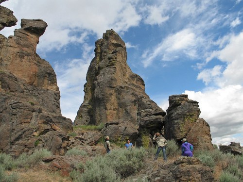 A group of people exploring rocky formations under a blue sky with scattered clouds.