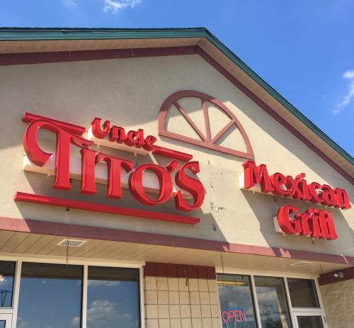 Sign for "Uncle Tito's Mexican Grill" on a building exterior, with a blue sky in the background.