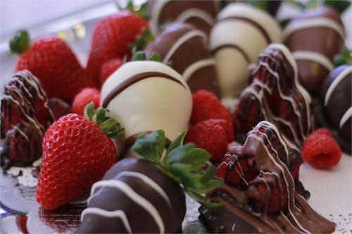A platter of chocolate-covered strawberries and raspberries, drizzled with white chocolate.