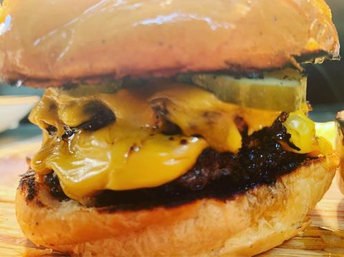 Close-up of a juicy cheeseburger with melted cheese, pickles, and a toasted bun on a wooden surface.