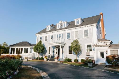 A large, light blue house with a white porch, surrounded by greenery and a clear blue sky.
