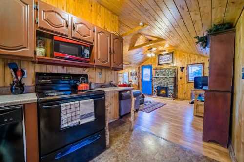 Cozy cabin interior featuring a kitchen, living area, and stone fireplace with wooden accents and warm lighting.