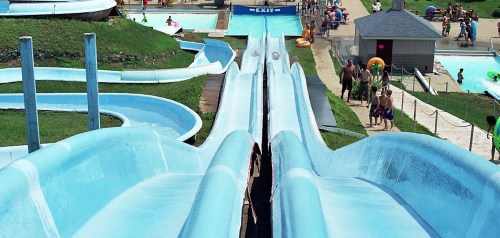 Two water slides at a water park, with people enjoying the pools and slides on a sunny day.