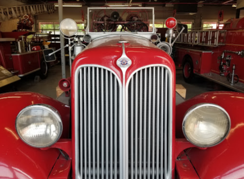 Close-up of a vintage red fire truck with chrome details, parked in a garage alongside other fire equipment.