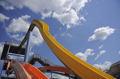 Colorful water slides against a blue sky with fluffy clouds, showcasing a fun water park attraction.