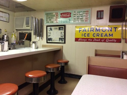 A retro diner interior with a counter, orange stools, and vintage ice cream and Coca-Cola signs on the walls.