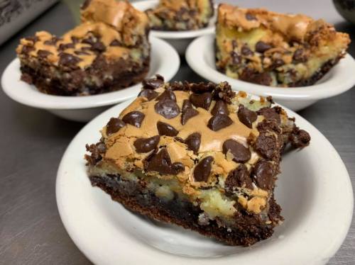 A close-up of chocolate chip dessert bars on small white plates, featuring a layered brownie and cookie topping.