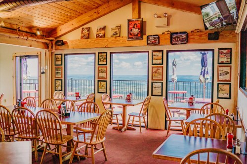 Cozy restaurant interior with wooden tables and chairs, large windows showcasing a scenic view, and vintage decor on the walls.