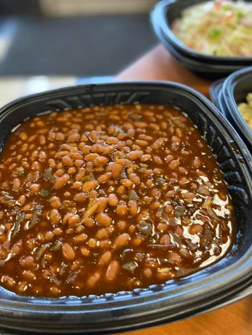A close-up of a black container filled with baked beans in a rich, brown sauce.