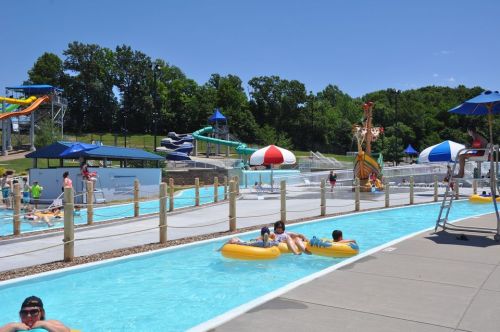 A sunny water park scene with slides, a lazy river, and people enjoying the water on inflatable tubes.