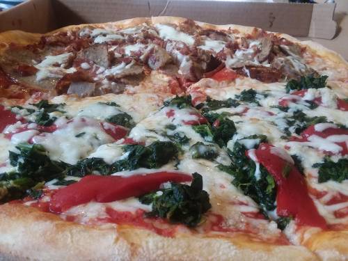 A pizza with two sections: one topped with meat and cheese, the other with spinach and red peppers on a golden crust.