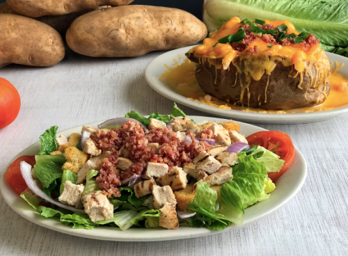 A fresh salad with grilled chicken, bacon, and tomatoes, alongside a cheesy loaded baked potato.