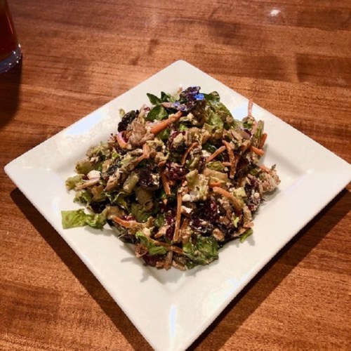 A colorful salad with mixed greens, shredded carrots, nuts, and a creamy dressing on a square white plate.
