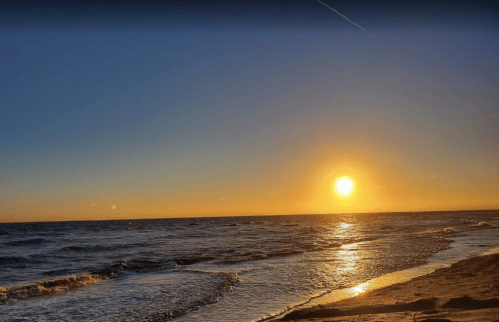 A serene beach scene at sunset, with golden sunlight reflecting on gentle waves and a clear sky.