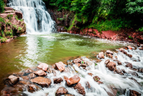 A serene waterfall cascading into a calm pool, surrounded by lush greenery and rocky terrain.