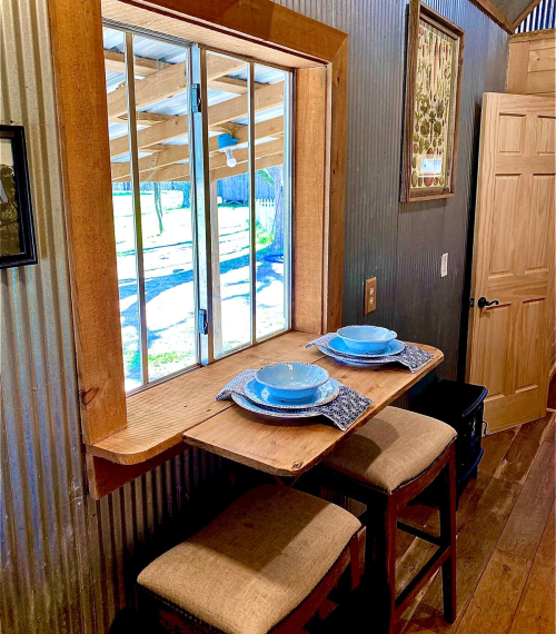 A cozy dining nook with a window, featuring a small table set for two with blue plates and stools.