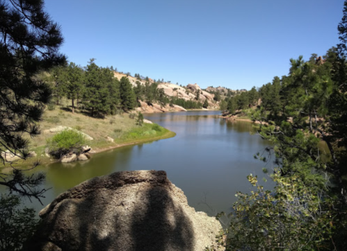A serene lake surrounded by trees and rocky hills under a clear blue sky.