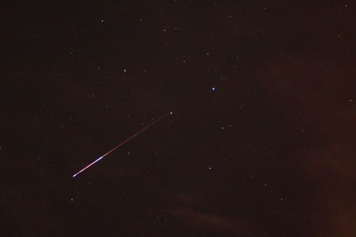 A meteor streaks across a starry night sky, with scattered stars visible in the dark background.