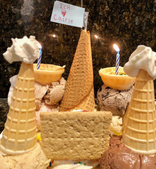 A creative ice cream castle made of cones, ice cream scoops, and a flag, with candles on top for decoration.