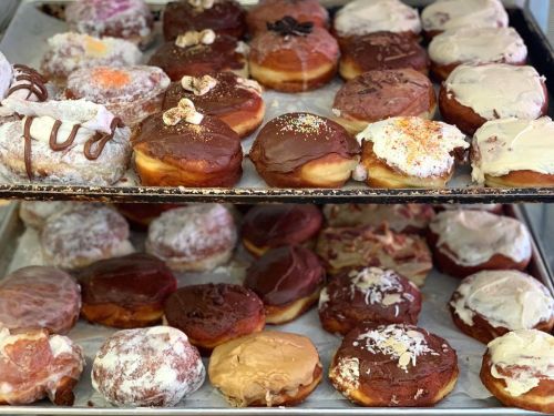 A display of assorted donuts with various toppings and glazes on two trays.