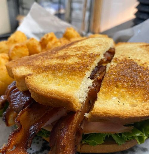 A close-up of a toasted sandwich filled with bacon and lettuce, served with crispy tater tots on the side.