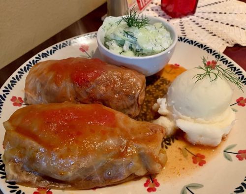 Two stuffed cabbage rolls with tomato sauce, served with mashed potatoes and a side of cucumber salad.