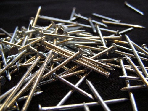 A close-up of a scattered pile of metal nails on a dark surface.