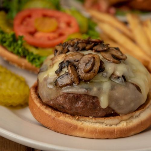 A juicy burger topped with melted cheese and mushrooms, served with lettuce, tomato, pickles, and fries on the side.